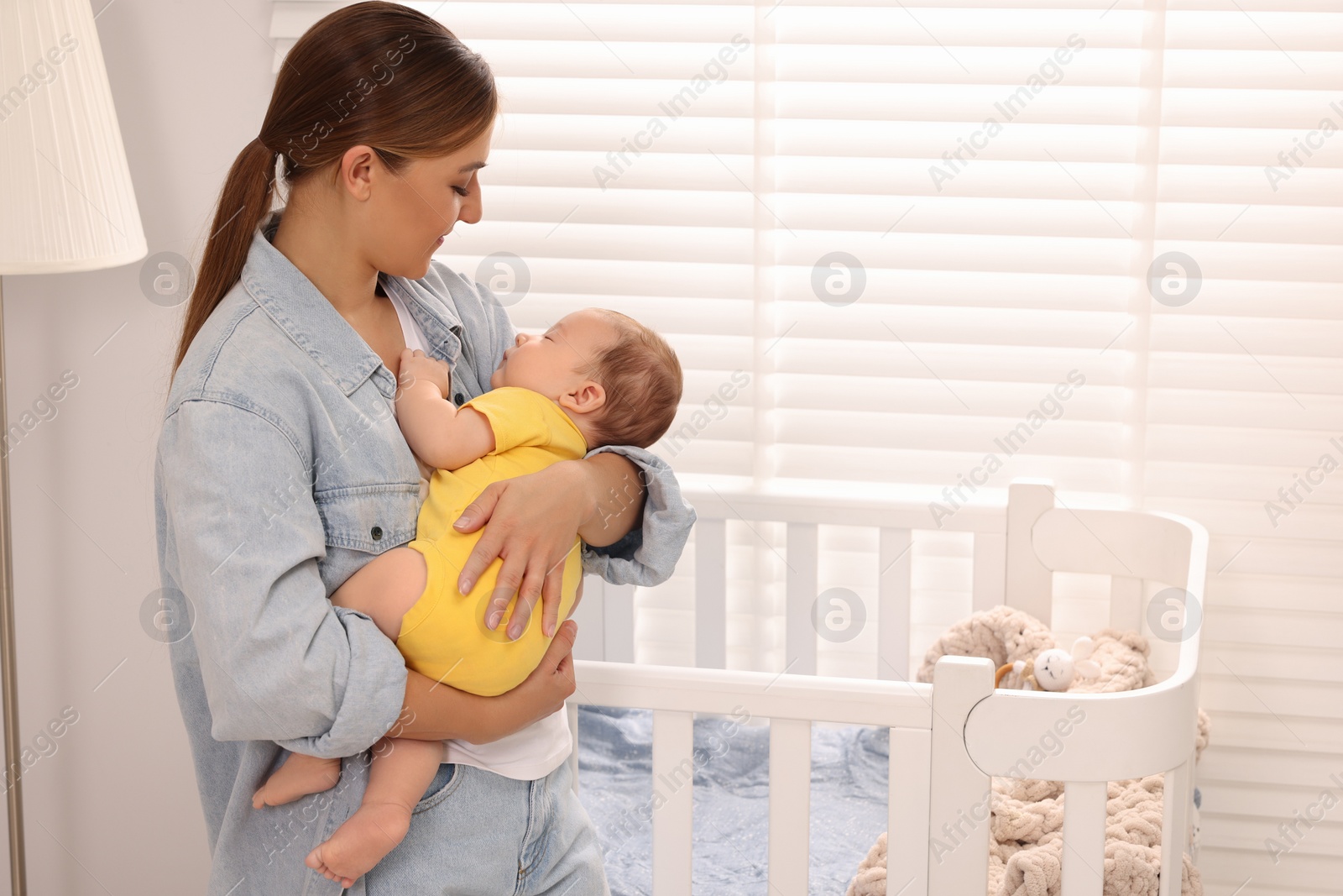 Photo of Mother holding her sleeping newborn baby in child's room, space for text