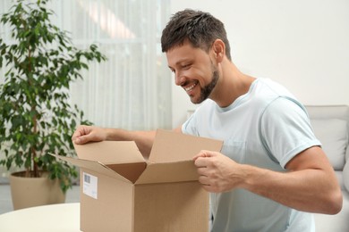Happy man opening parcel at home. Internet shopping