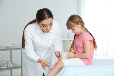 Photo of Female doctor cleaning little girl's leg injury in clinic. First aid