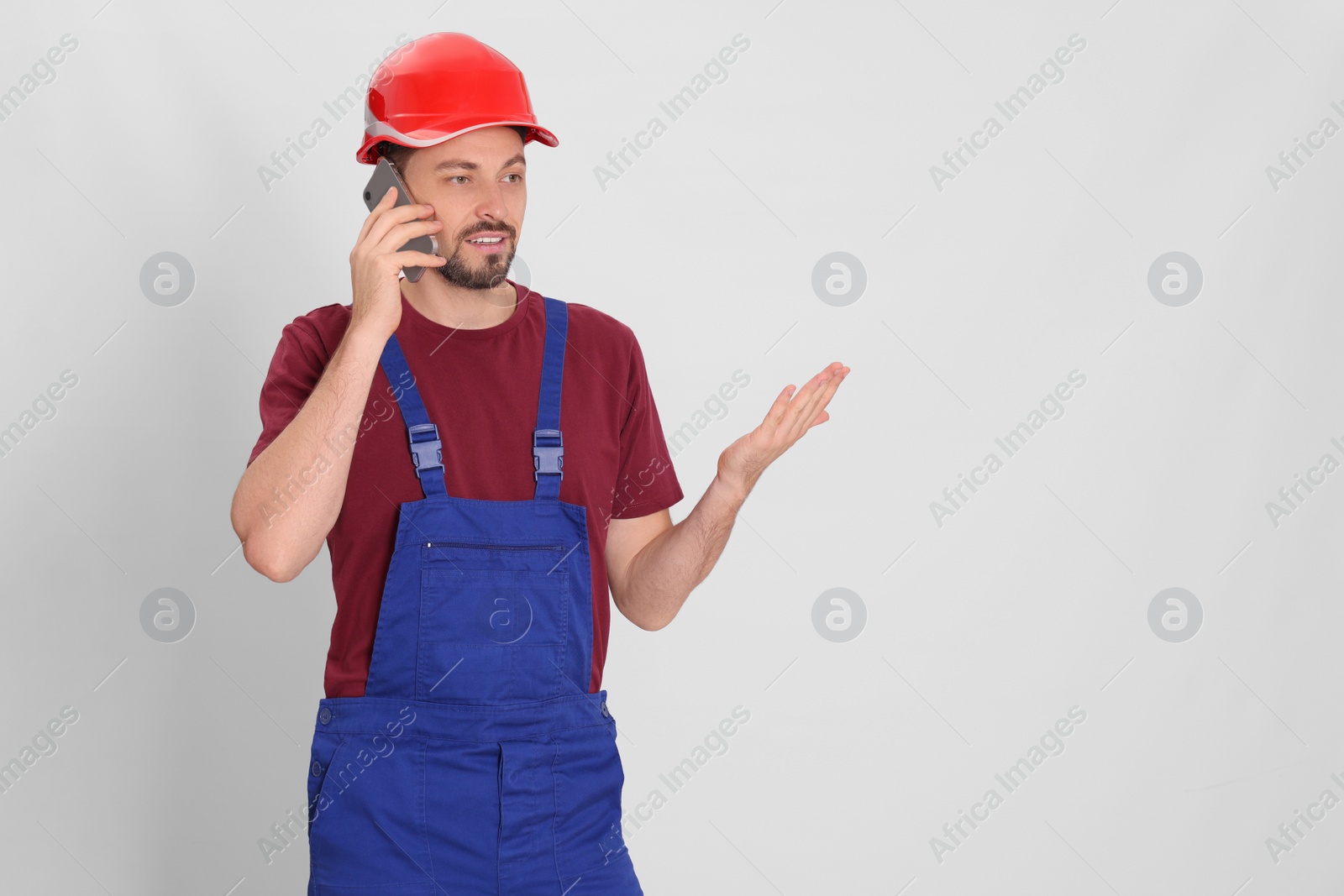 Photo of Professional repairman in uniform talking on phone against white background, space for text