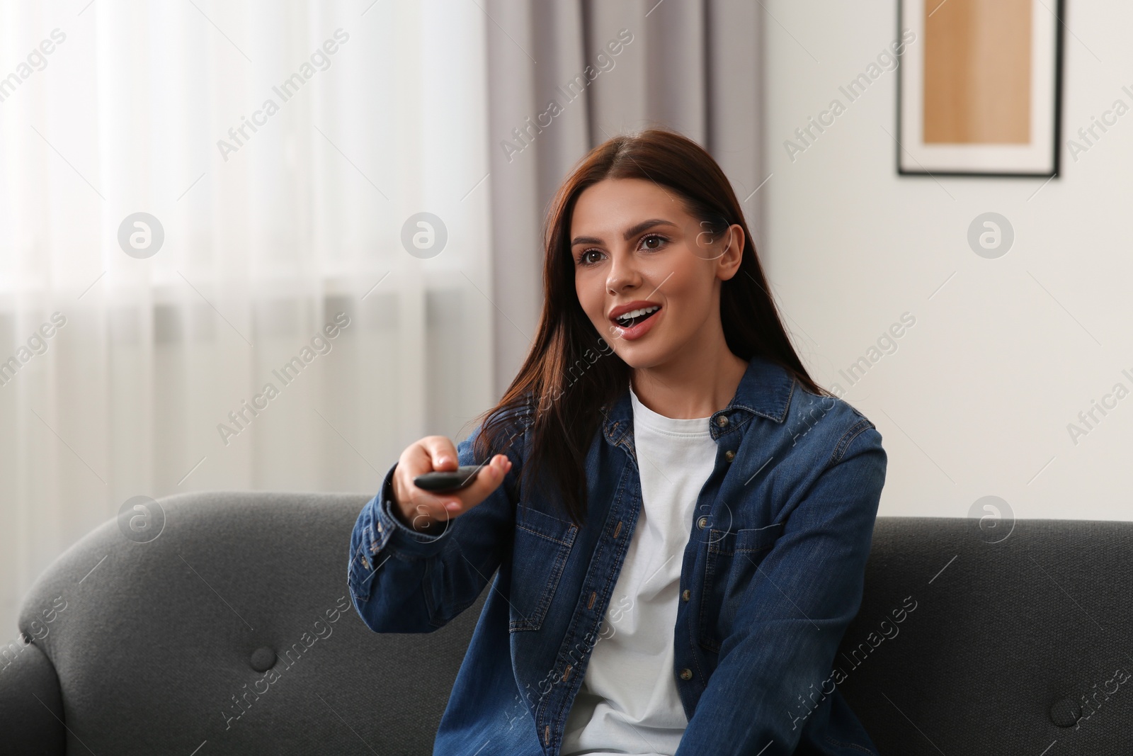 Photo of Beautiful woman changing TV channels with remote control on sofa at home