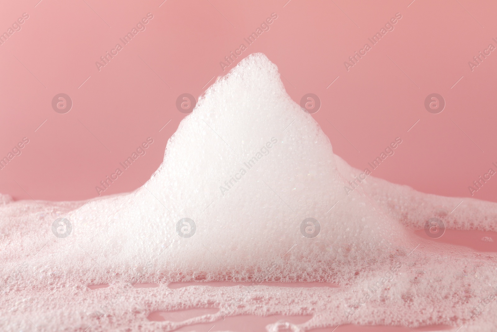 Photo of Fluffy bath foam on pink background, closeup. Care product