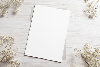 Photo of Empty sheet of paper and gypsophila flowers on white wooden table, flat lay. Mockup for design