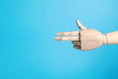 Wooden mannequin hand on light blue background. Space for text