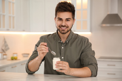 Photo of Happy young man with tasty yogurt at table in kitchen