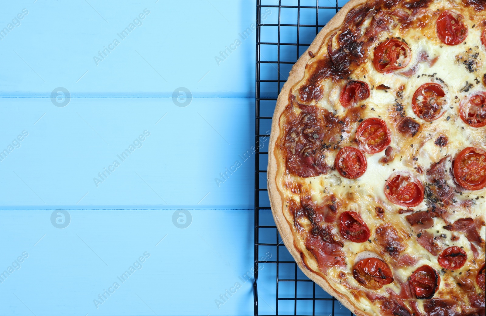 Photo of Delicious homemade quiche with prosciutto and tomatoes on light blue wooden table, top view. Space for text