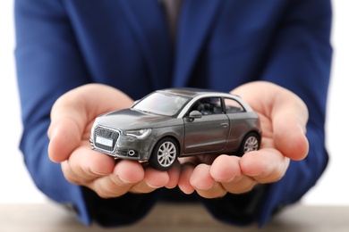 Photo of Insurance agent holding toy car over table, focus on hands