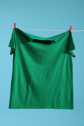 Photo of One green t-shirt drying on washing line against light blue background