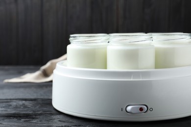 Photo of Modern yogurt maker with full jars on black wooden table