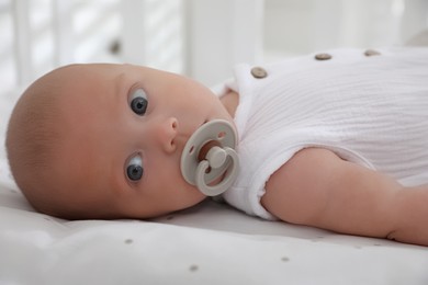 Photo of Cute little baby with pacifier lying on bed, closeup