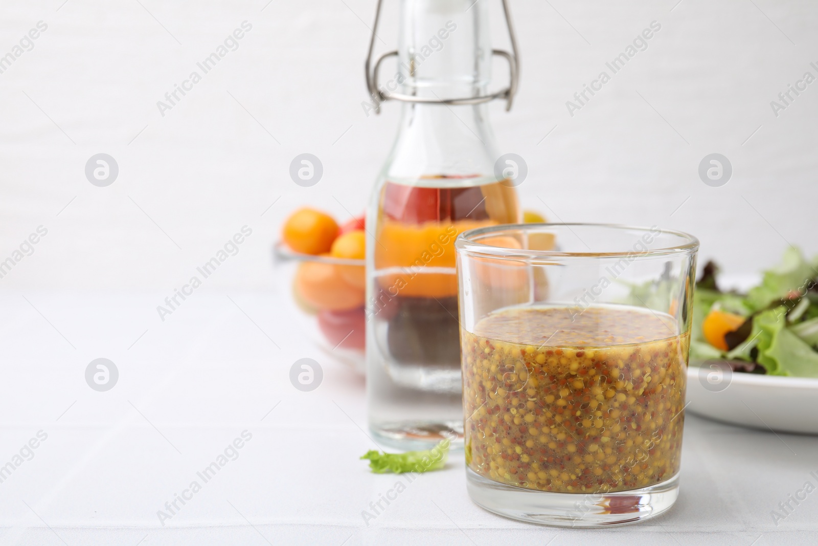 Photo of Tasty vinegar based sauce (Vinaigrette) in glass on light tiled table, closeup. Space for text