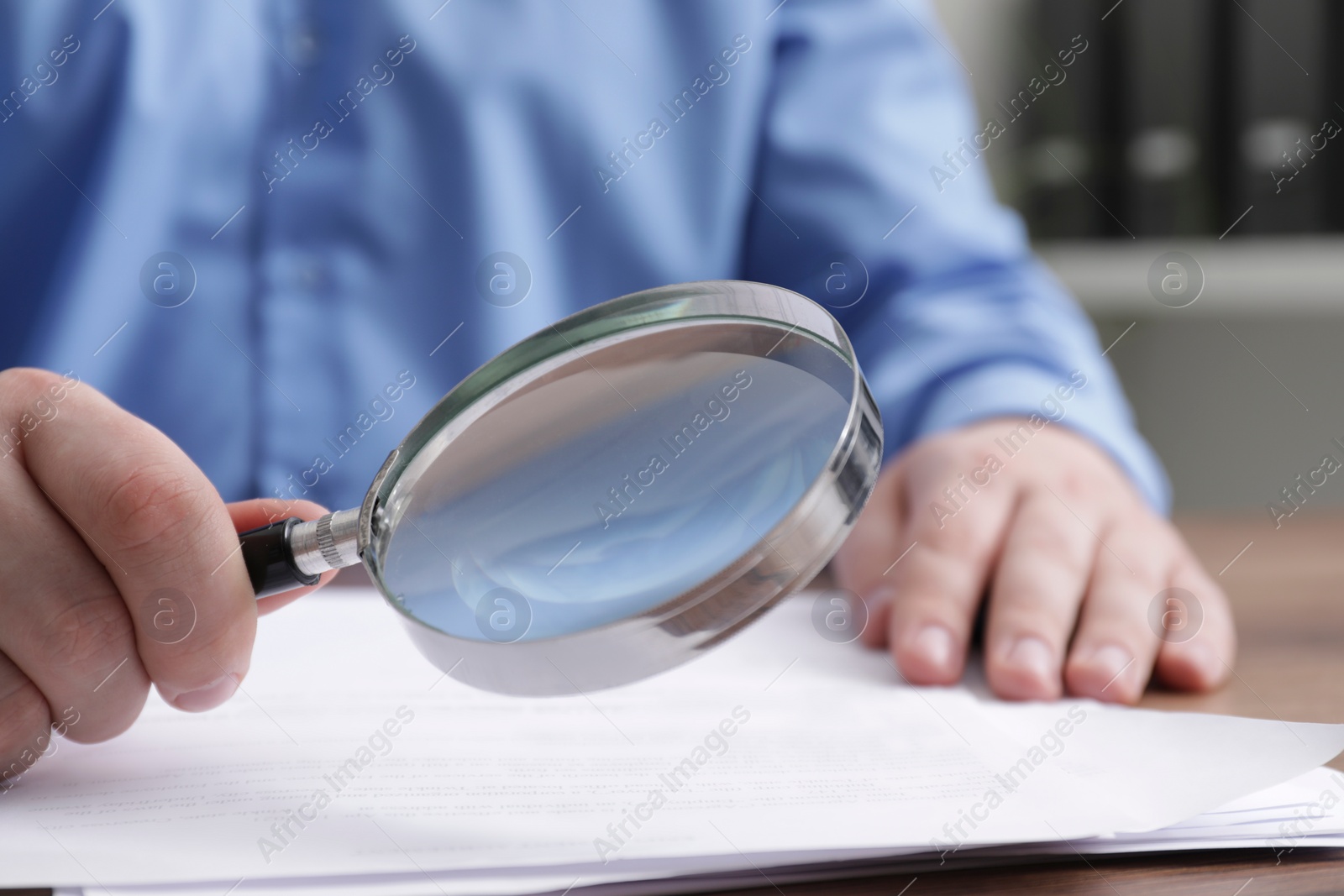 Photo of Man looking at document through magnifier at wooden table, closeup. Searching concept