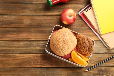 Lunch box with appetizing food and notebooks on wooden table