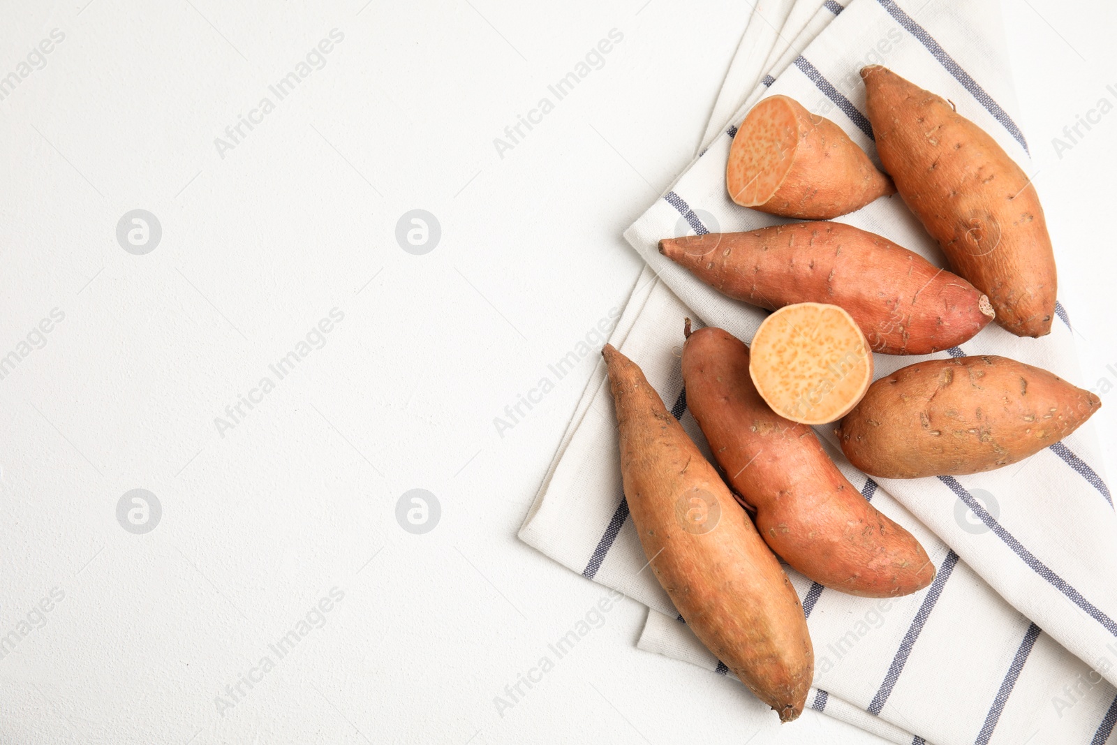Photo of Whole and cut ripe sweet potatoes on white table, top view. Space for text