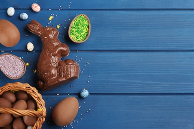 Photo of Chocolate Easter bunny and eggs on blue wooden table, flat lay. Space for text