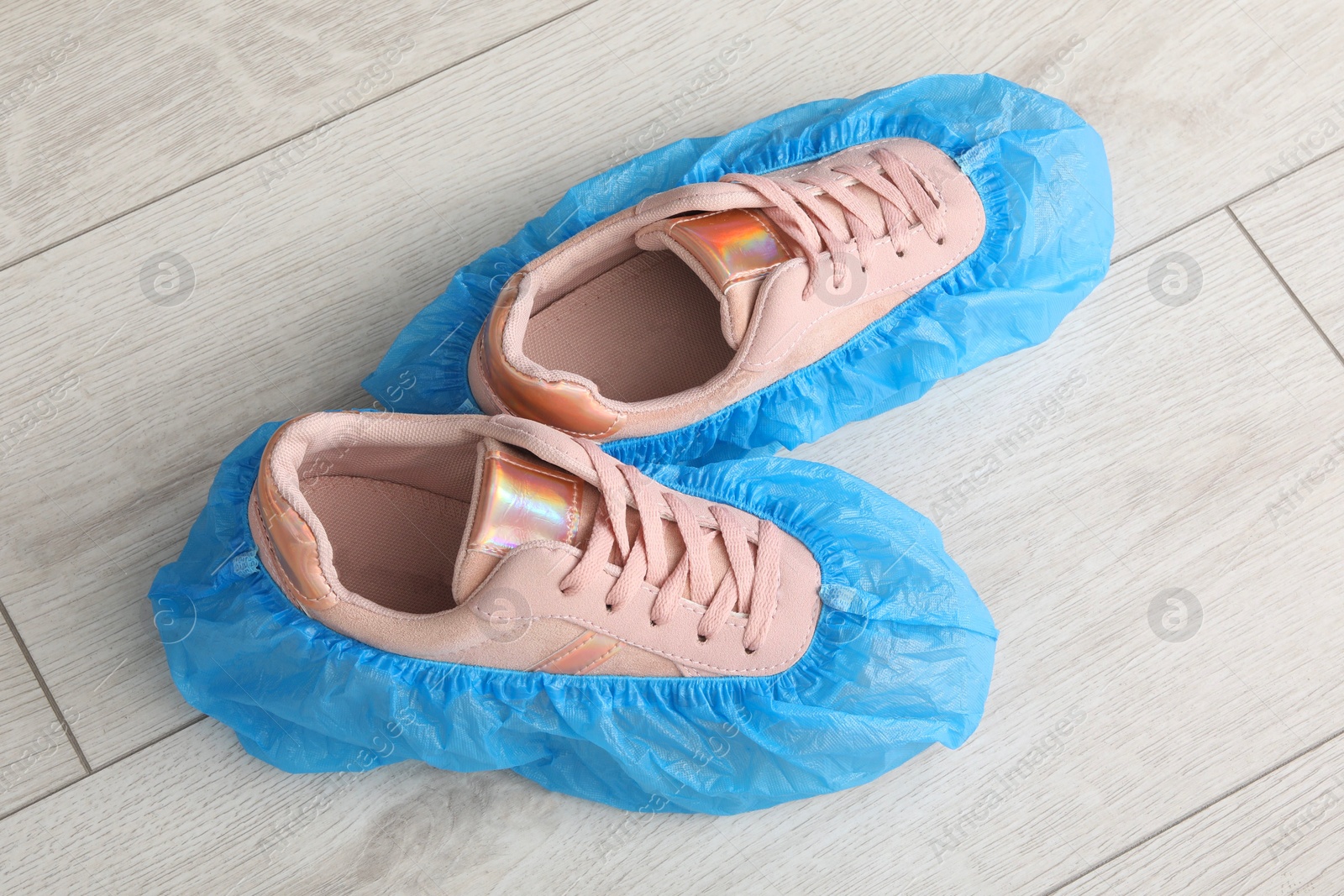 Photo of Women`s sneakers in blue shoe covers on light wooden floor, top view