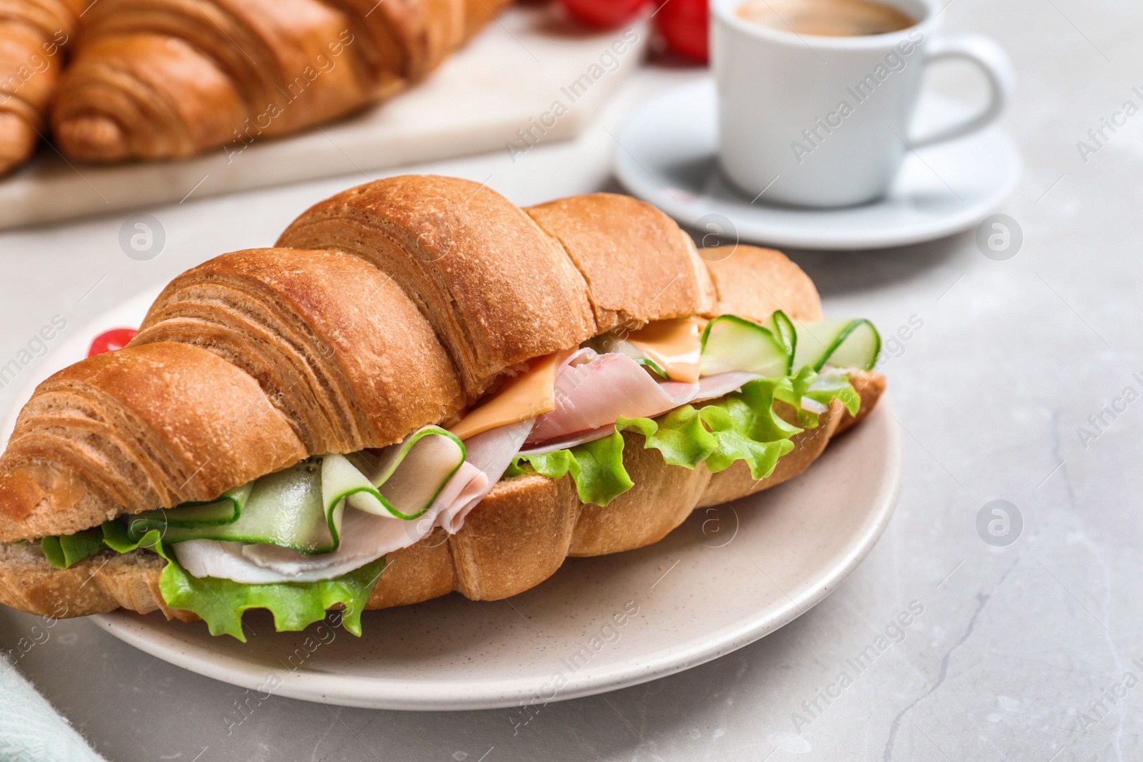 Photo of Tasty croissant sandwich with ham and cucumber on light table, closeup