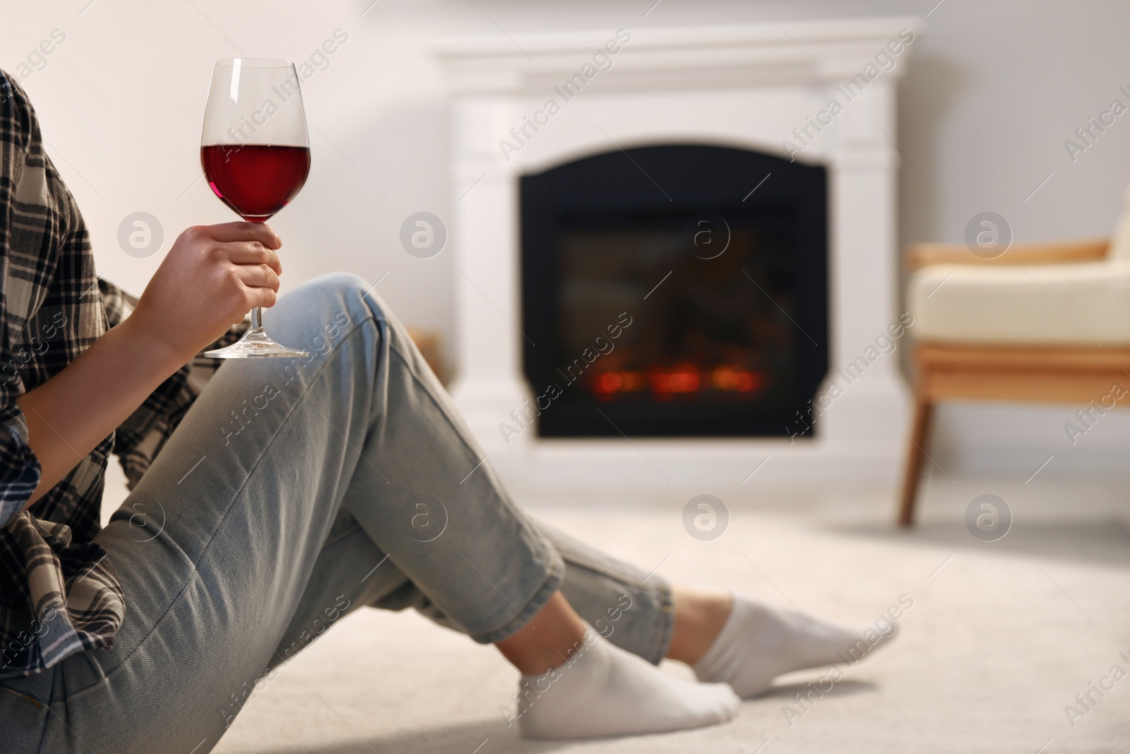 Photo of Young woman with glass of wine resting near fireplace at home, closeup