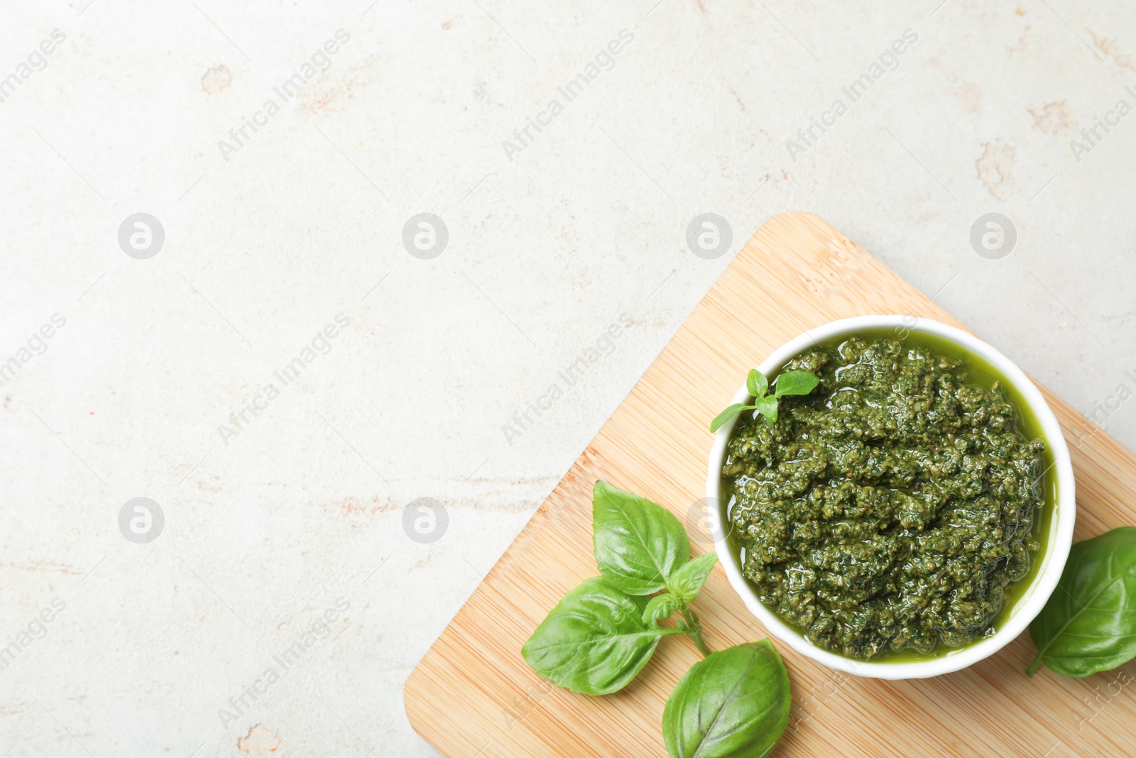 Photo of Board with homemade basil pesto sauce in bowl on table, top view. Space for text