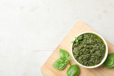 Photo of Board with homemade basil pesto sauce in bowl on table, top view. Space for text