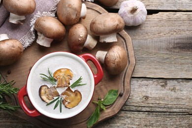 Photo of Delicious homemade mushroom soup in ceramic pot and fresh ingredients on wooden table, flat lay. Space for text