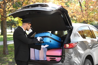 Photo of Young driver loading suitcases into car trunk outdoors