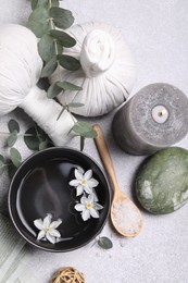 Flat lay composition with herbal massage bags, spa products and flowers on light grey table