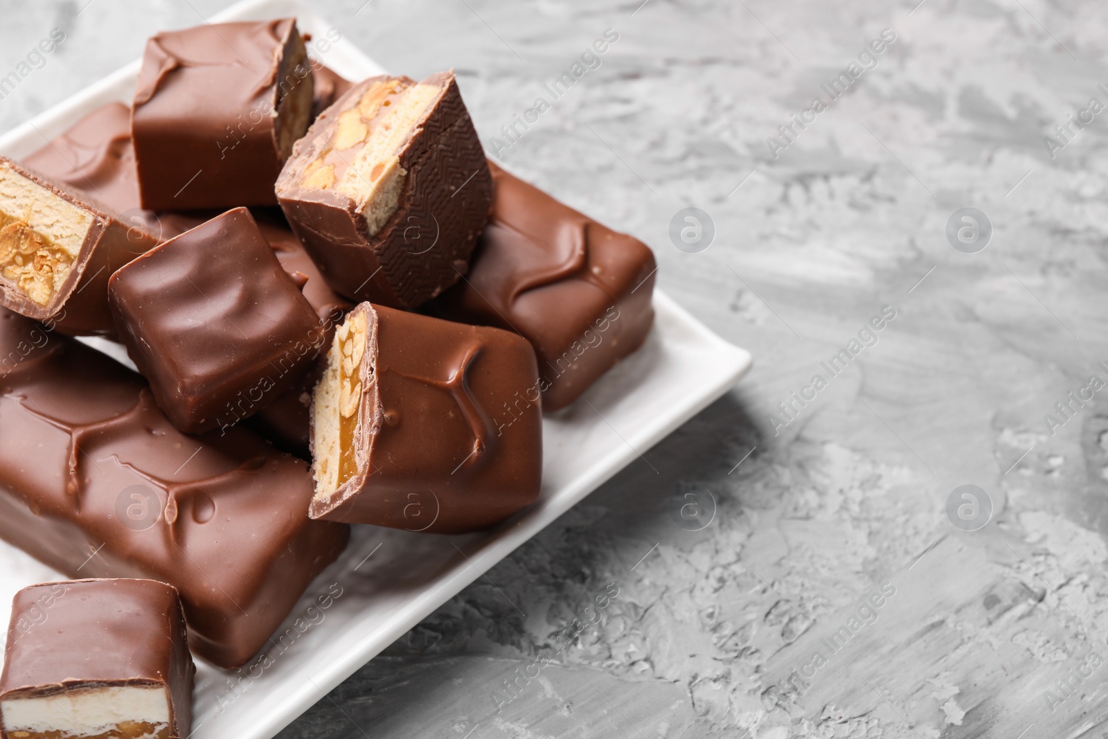 Photo of Tasty chocolate bars with nougat, caramel and nuts on gray textured table, closeup. Space for text