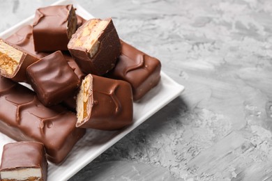 Photo of Tasty chocolate bars with nougat, caramel and nuts on gray textured table, closeup. Space for text