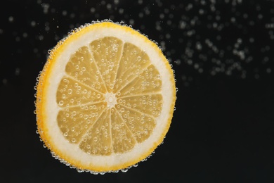 Photo of Slice of lemon in sparkling water on black background, space for text. Citrus soda