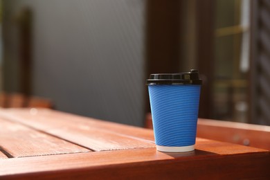 Photo of Takeaway paper coffee cup on wooden table outdoors, space for text