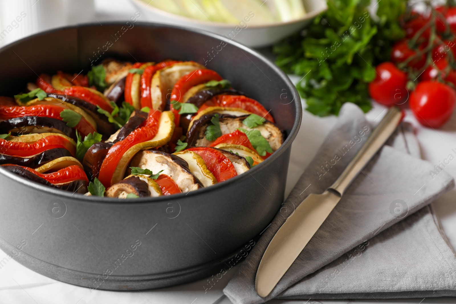 Photo of Delicious ratatouille in round baking pan and knife on table, closeup