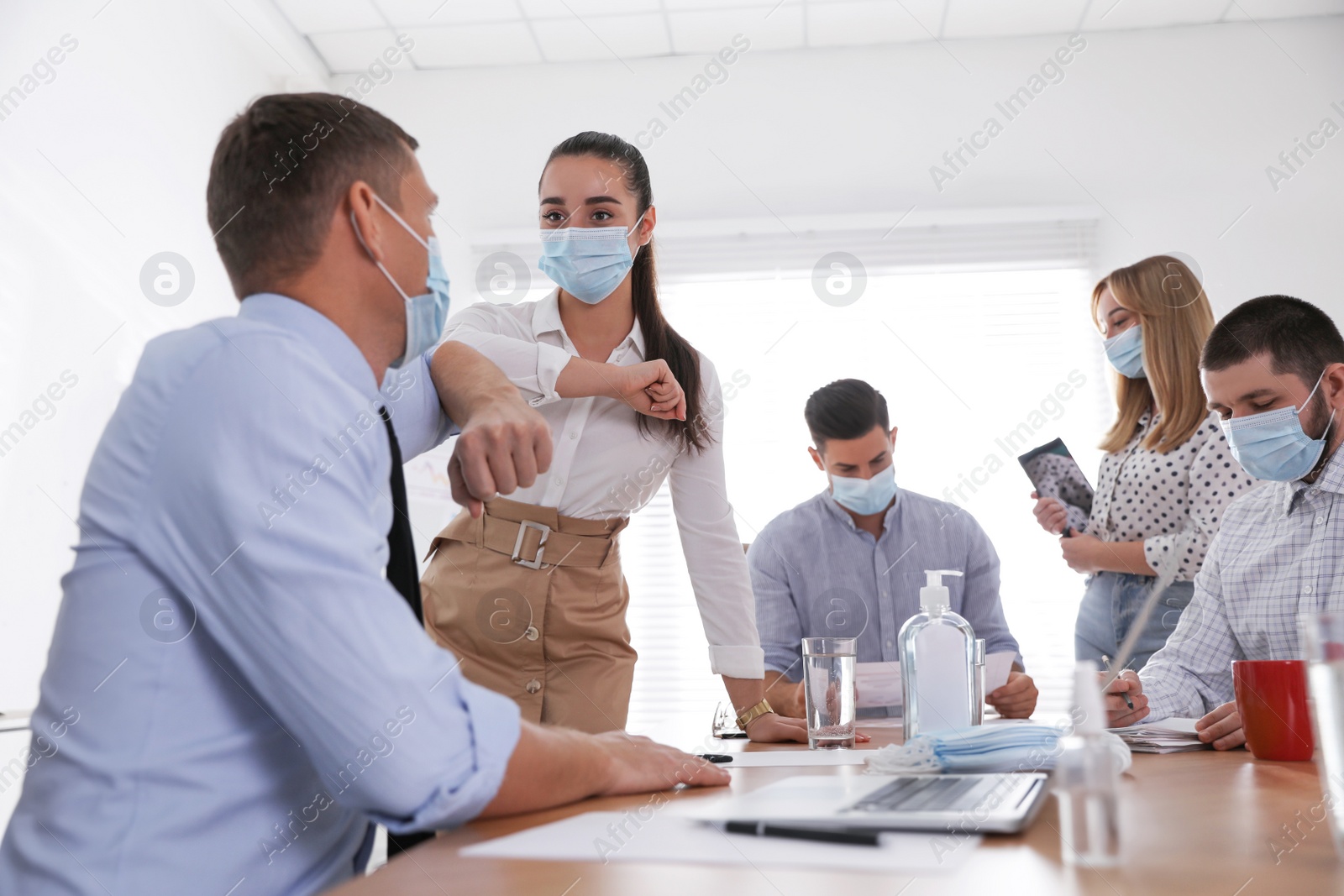 Photo of Coworkers with protective masks making elbow bump in office. Informal greeting during COVID-19 pandemic