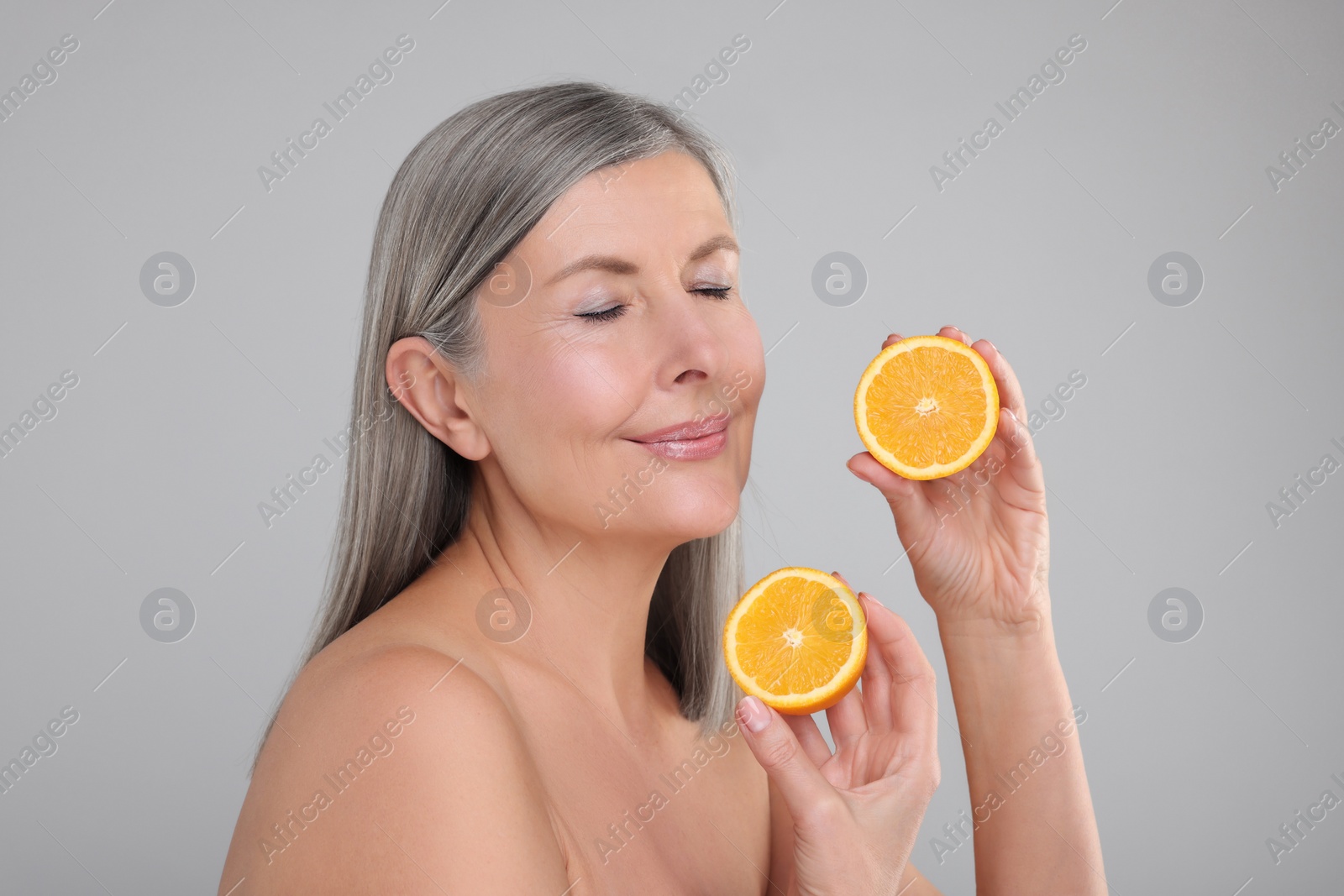 Photo of Beautiful woman with halves of orange rich in vitamin C on grey background