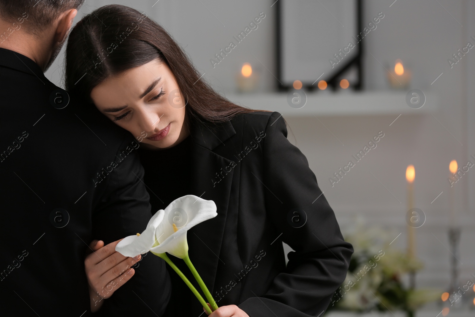 Photo of Sad couple with calla lily flowers mourning indoors, space for text. Funeral ceremony