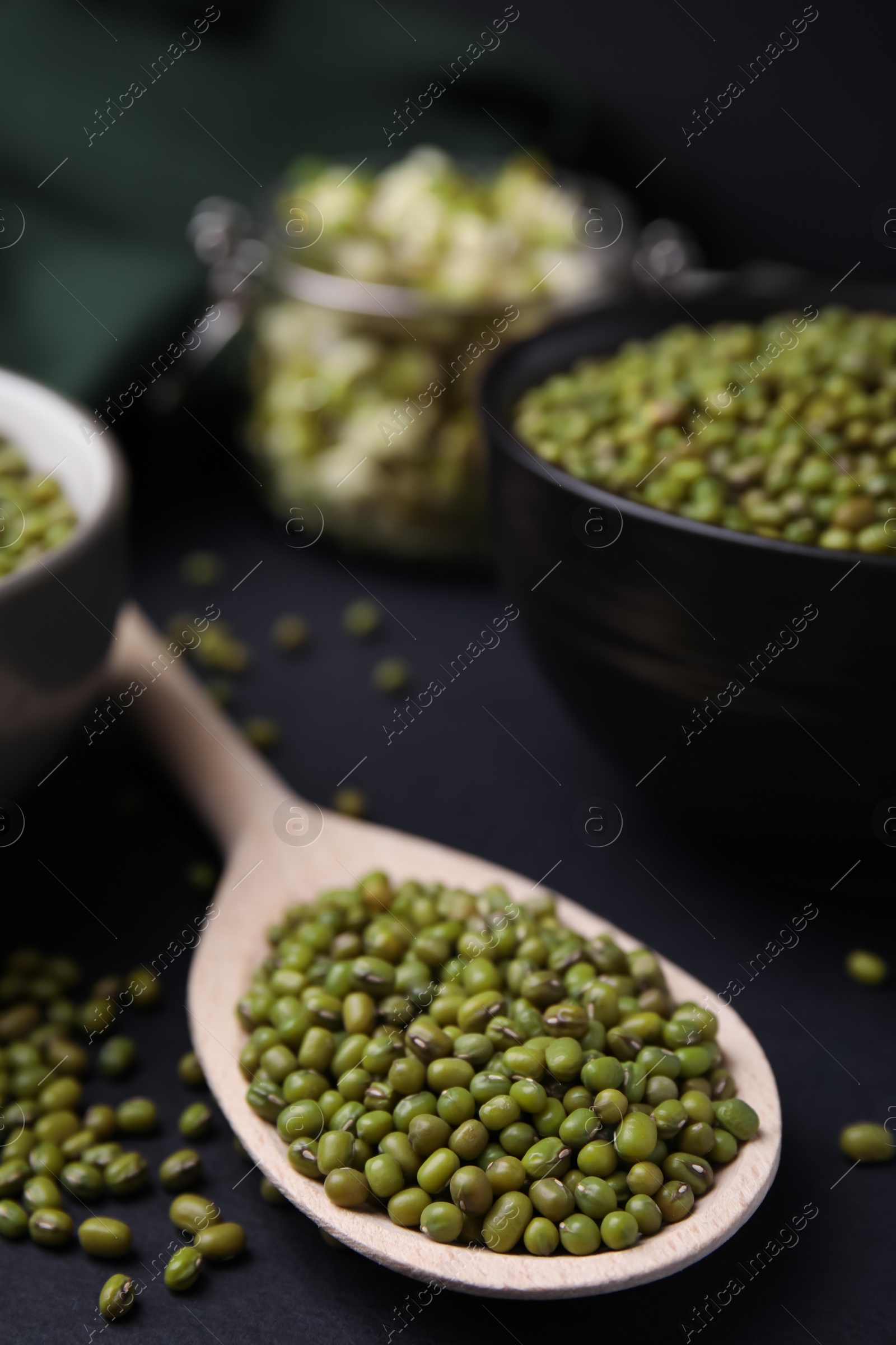 Photo of Different dishware with green mung beans on black background, closeup