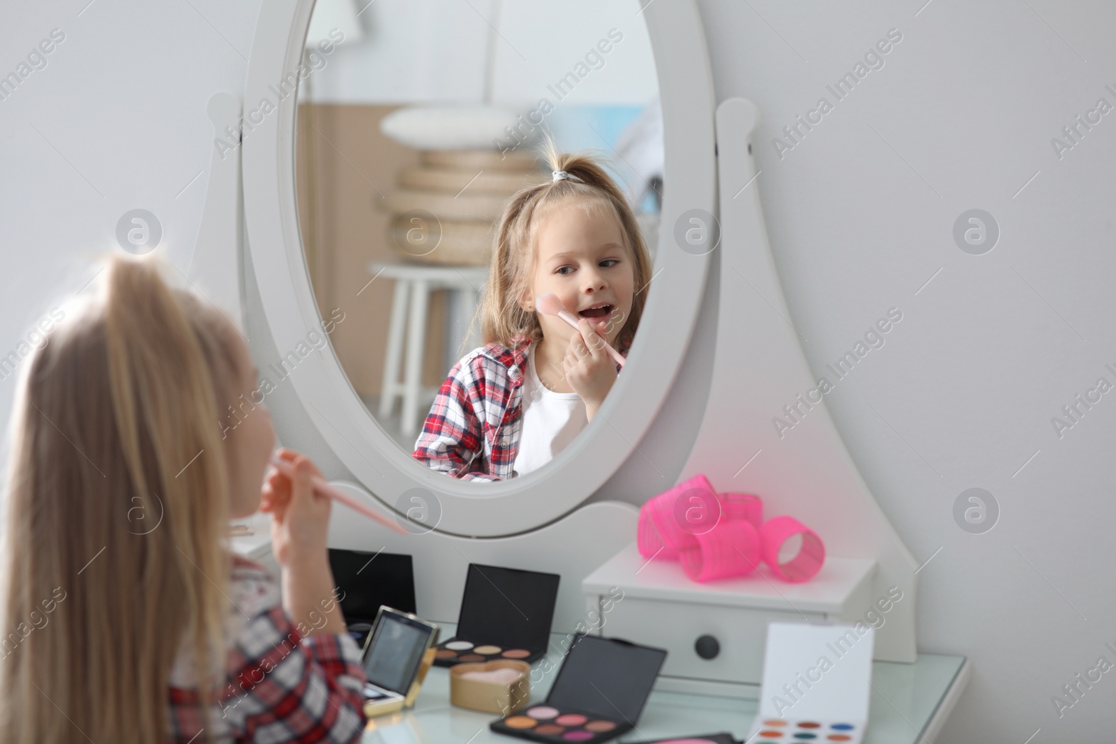 Photo of Adorable little girl applying makeup at dressing table indoors