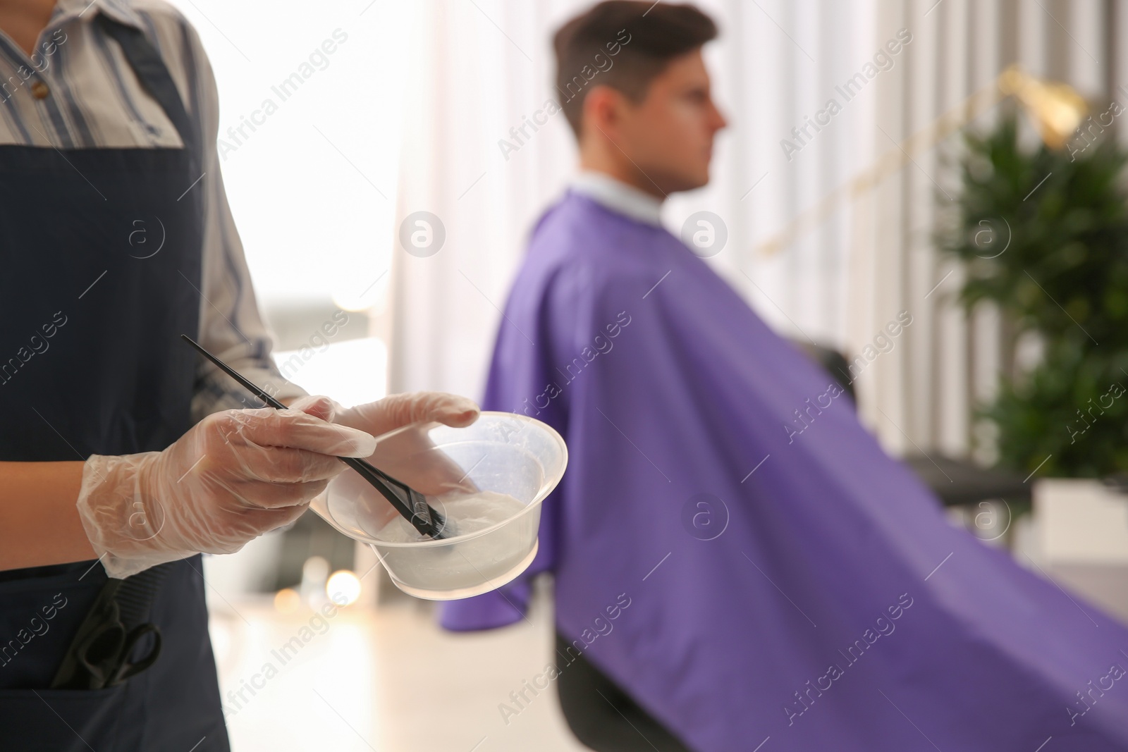 Photo of Professional hairdresser holding bowl with hair dye in beauty salon, closeup