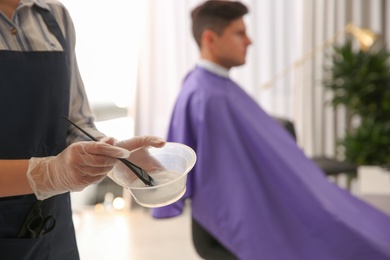 Professional hairdresser holding bowl with hair dye in beauty salon, closeup