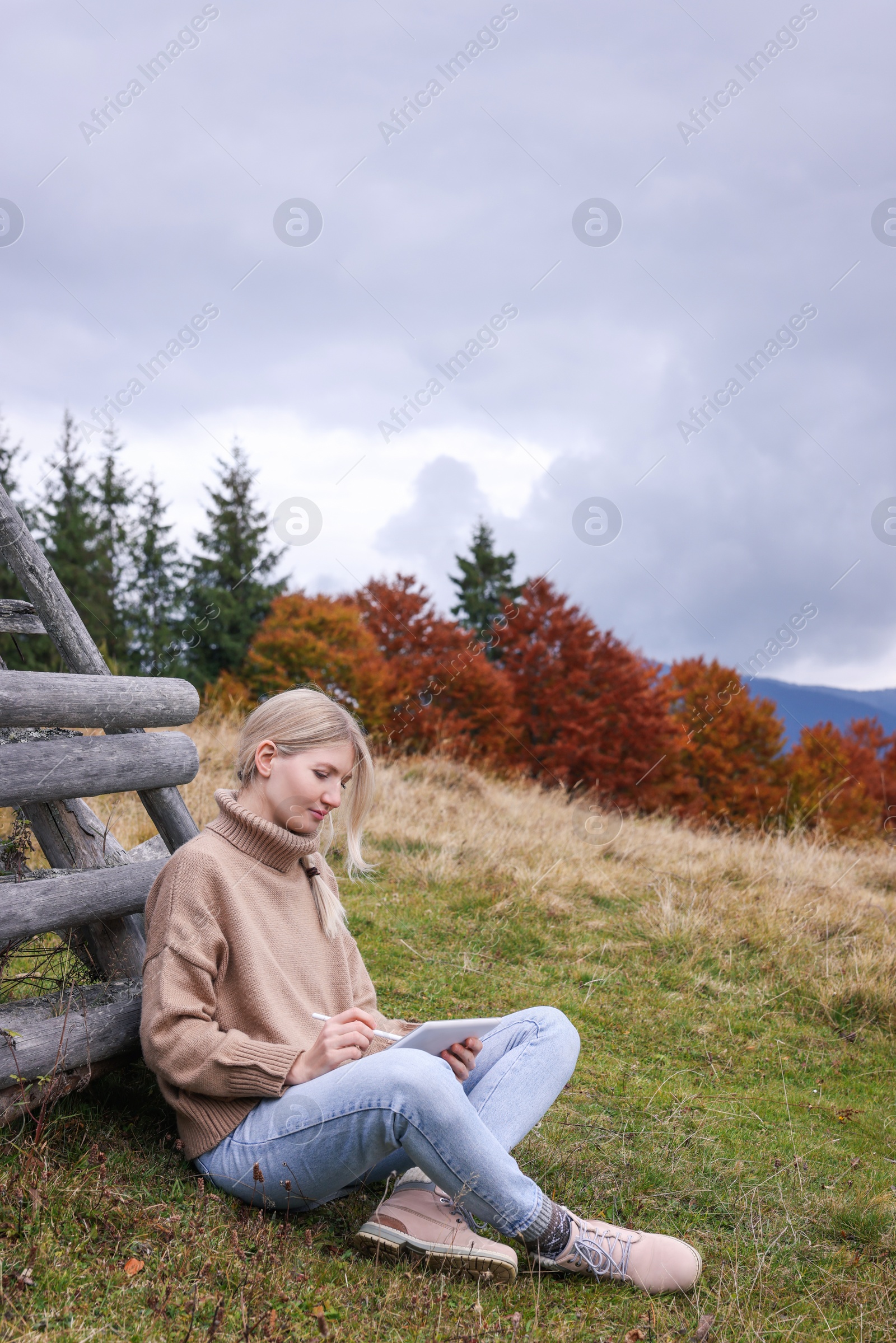 Photo of Young woman drawing on tablet in mountains, space for text