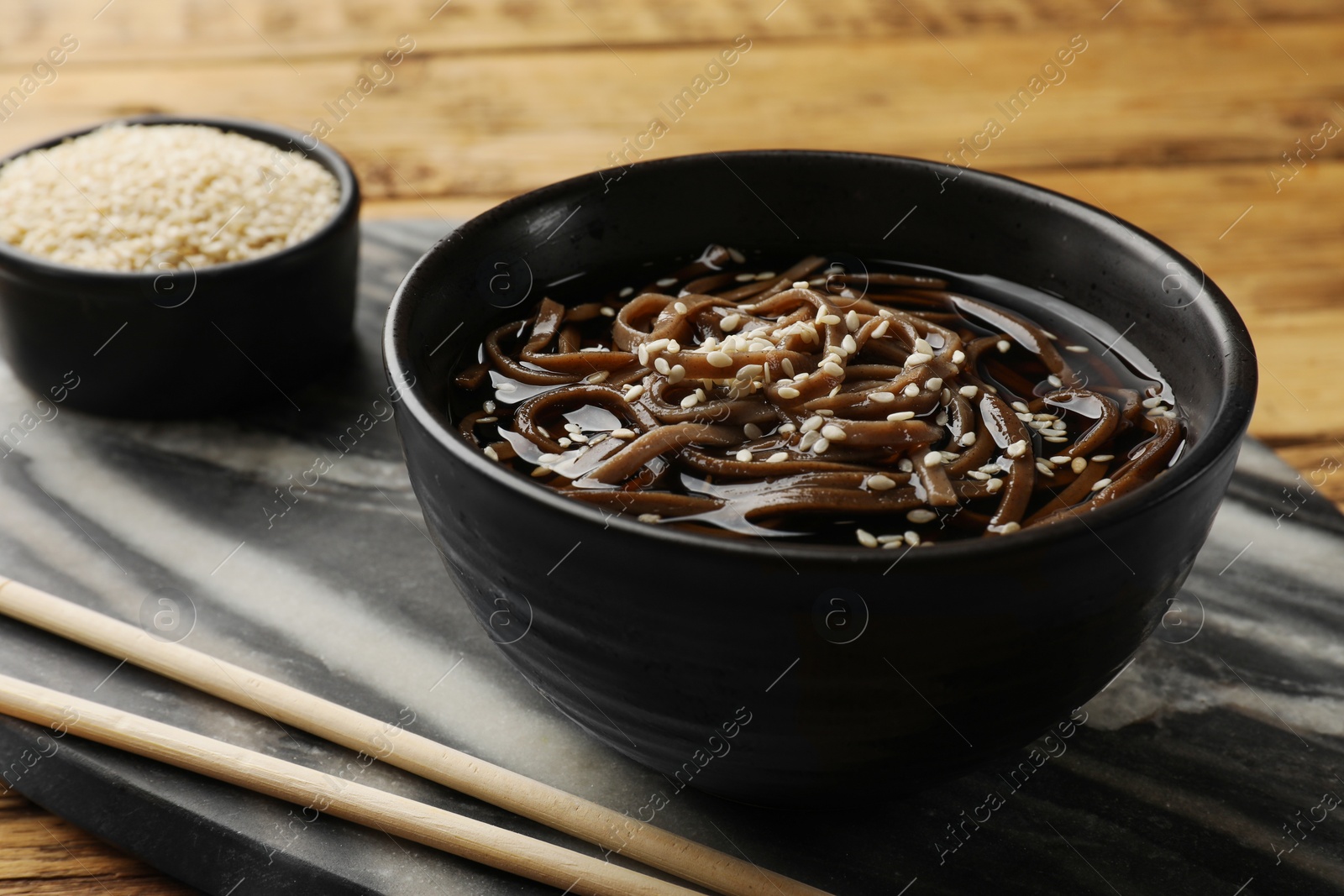 Photo of Tasty soup with buckwheat noodles (soba), sesame and chopsticks on table, closeup