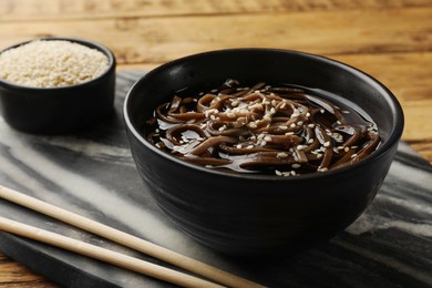 Photo of Tasty soup with buckwheat noodles (soba), sesame and chopsticks on table, closeup