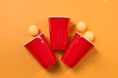 Photo of Plastic cups and balls for beer pong on orange background, flat lay