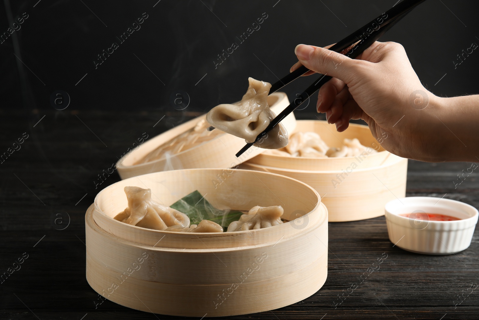 Photo of Woman cooking tasty baozi dumplings in bamboo steamer at table, closeup