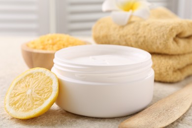 Body care. Composition with moisturizing cream in open jar and half of lemon on light textured table, closeup