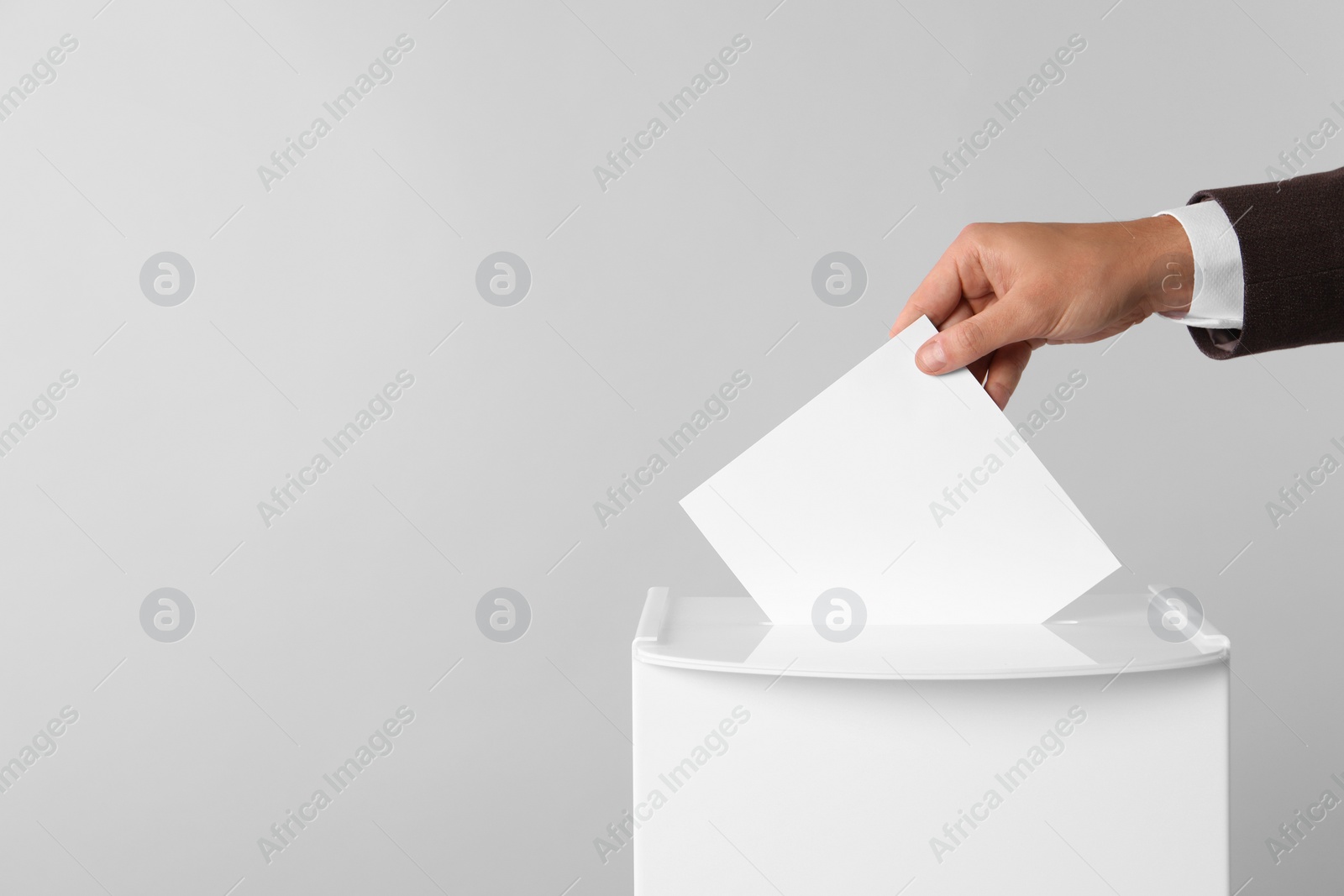 Photo of Man putting his vote into ballot box on light grey background, closeup. Space for text