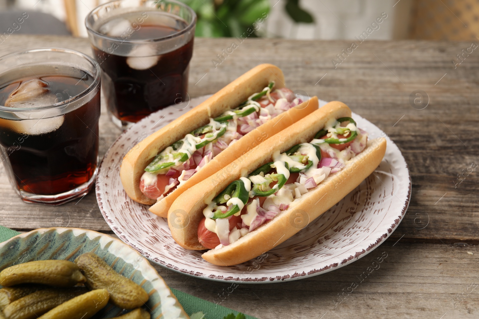 Photo of Delicious hot dogs with onion, chili pepper and sauce served on wooden table