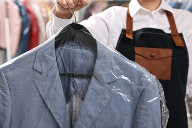 Photo of Dry-cleaning service. Woman holding jacket in plastic bag indoors, closeup