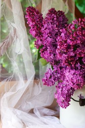 Photo of Beautiful lilac flowers in milk can near window indoors, closeup