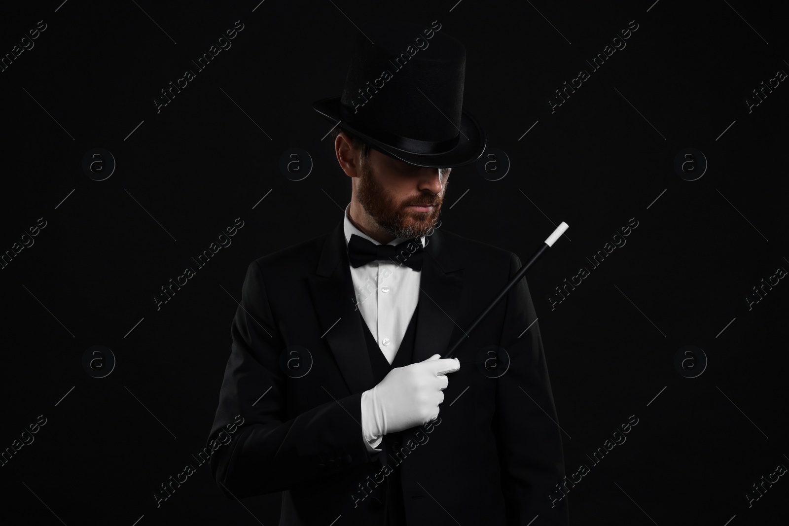 Photo of Magician in top hat holding wand on black background